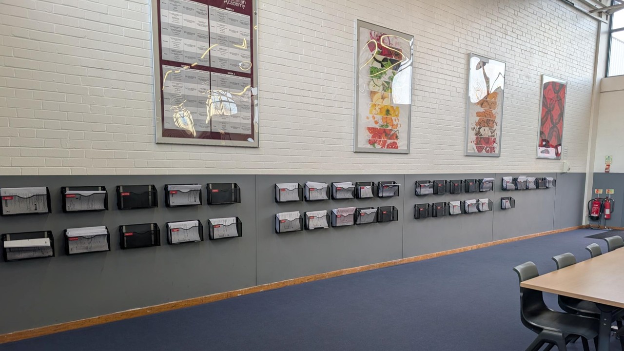 Wall-mounted racks holding past papers for each subject in the Macmillan Academy dining hall